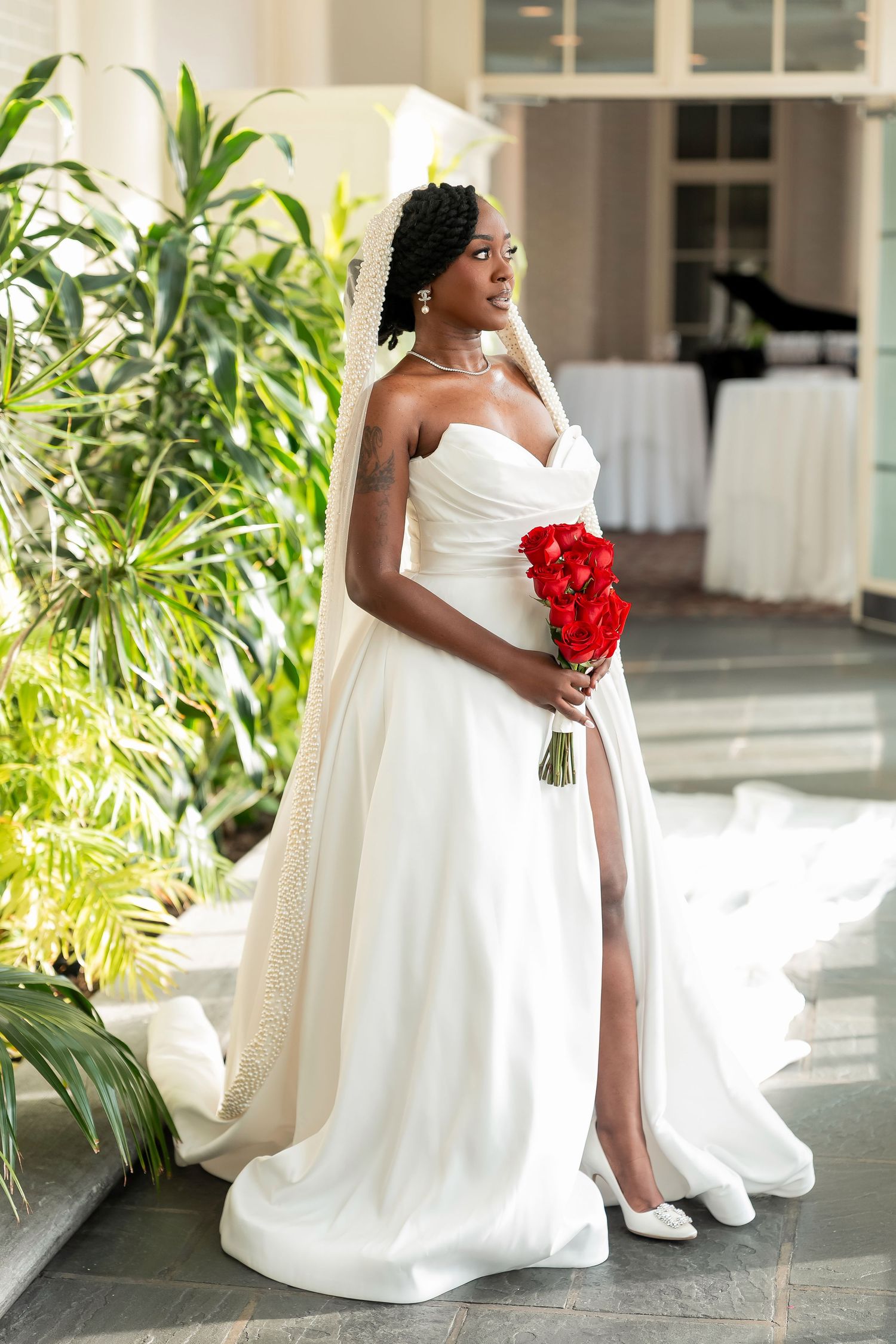 Elegant Black bride in strapless white gown with slit, lace veil, and red rose bouquet posing indoors. Deerfield Golf Club Newark De