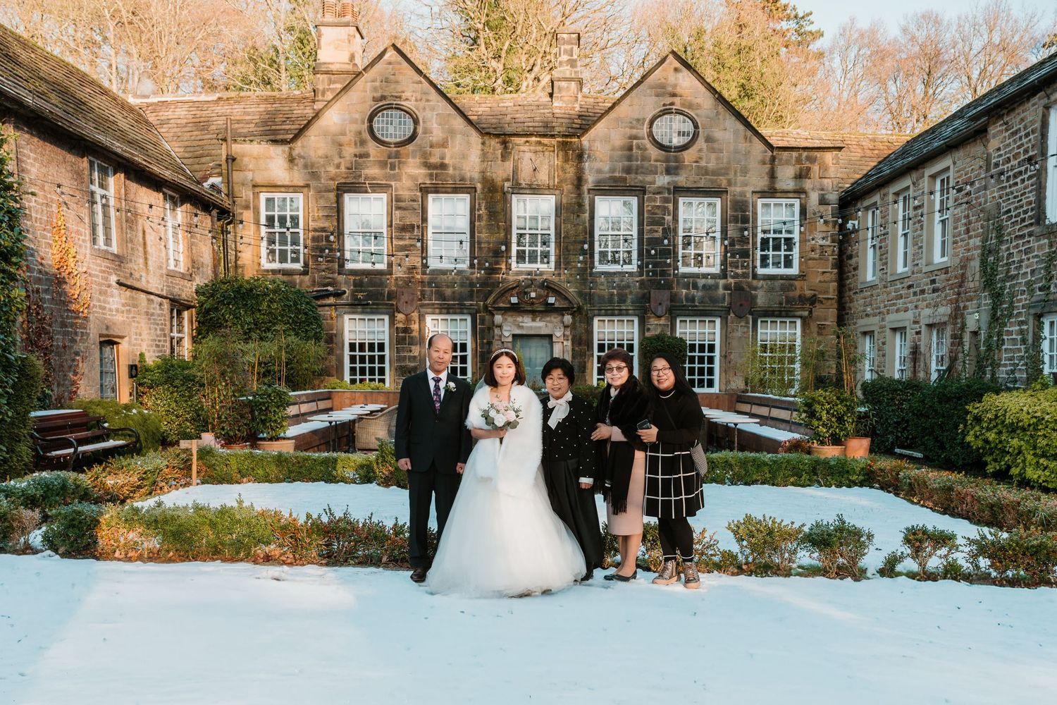 Wedding party poses in snow outside historic stone manor in winter. Whitley Hall Wedding