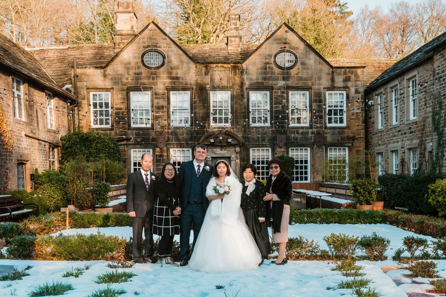 Wedding party posing in snow outside a historic stone manor house in winter. Whitley Hall Wedding