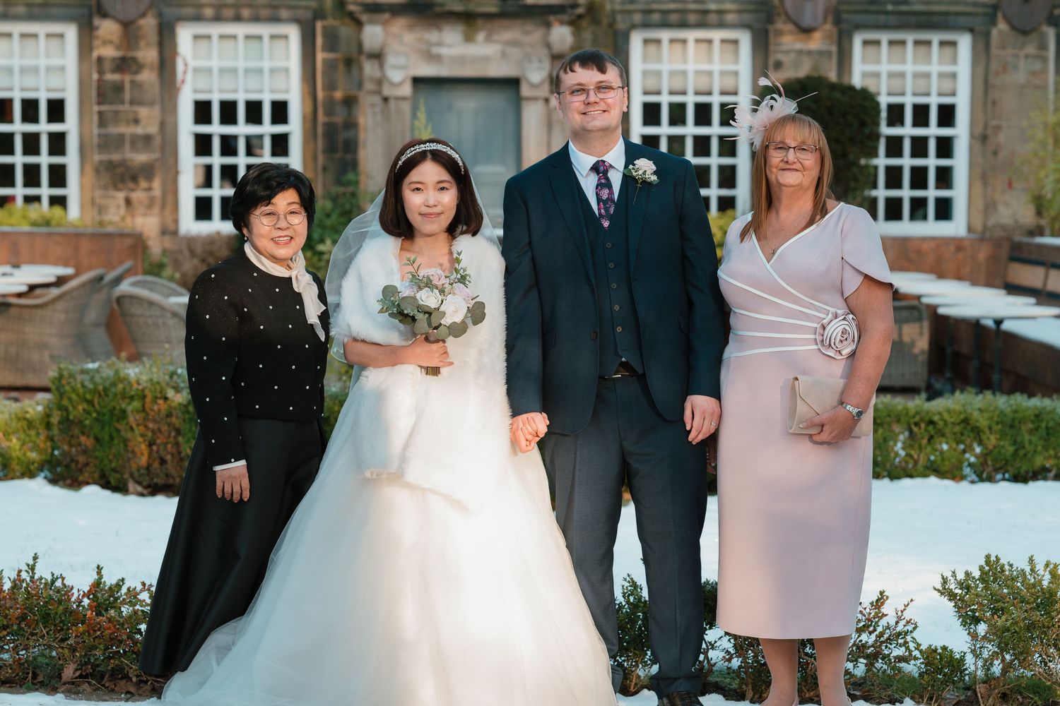 Bride and groom pose with two female guests in snowy winter wedding venue garden. Whitley Hall Wedding