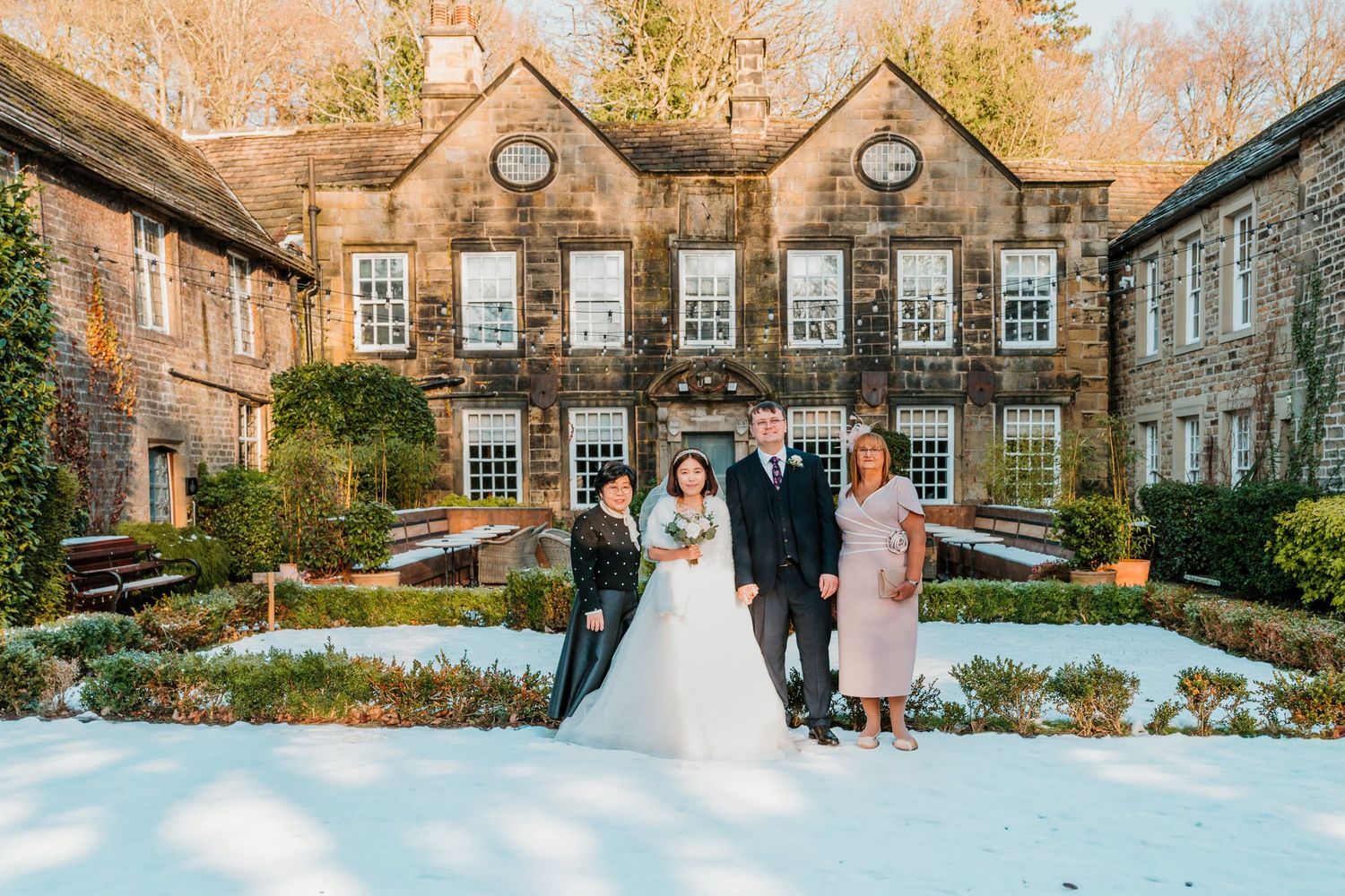 Wedding party of five poses in snowy garden outside historic stone manor house. Whitley Hall Wedding
