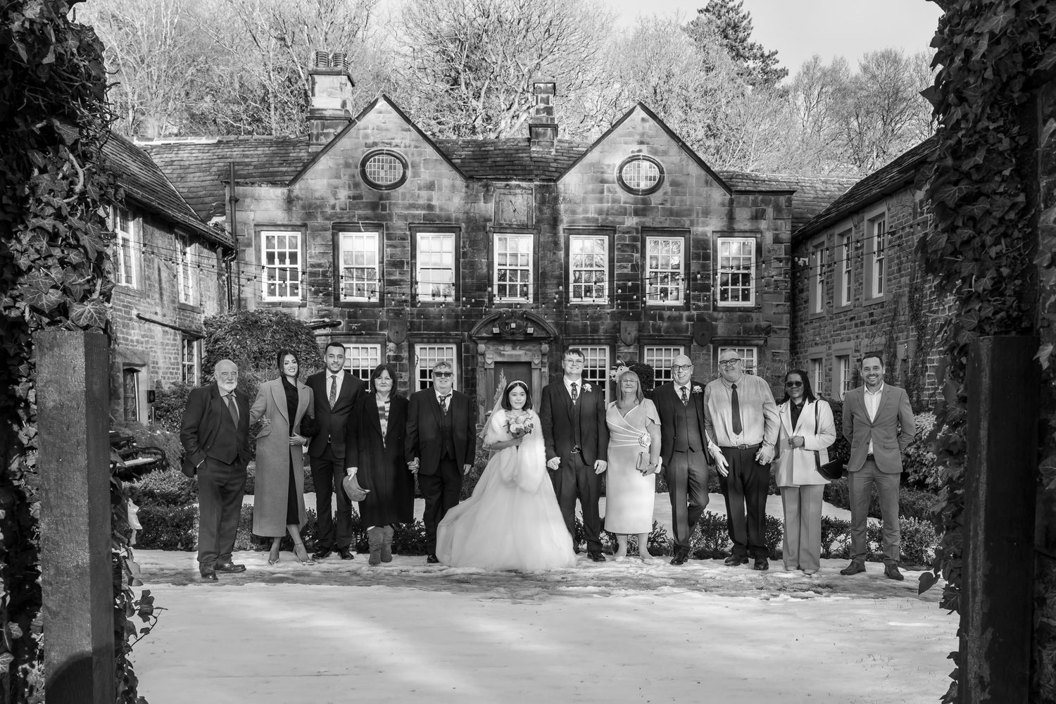Black and white wedding photo of bride, groom, and guests posing in front of an elegant country house venue.