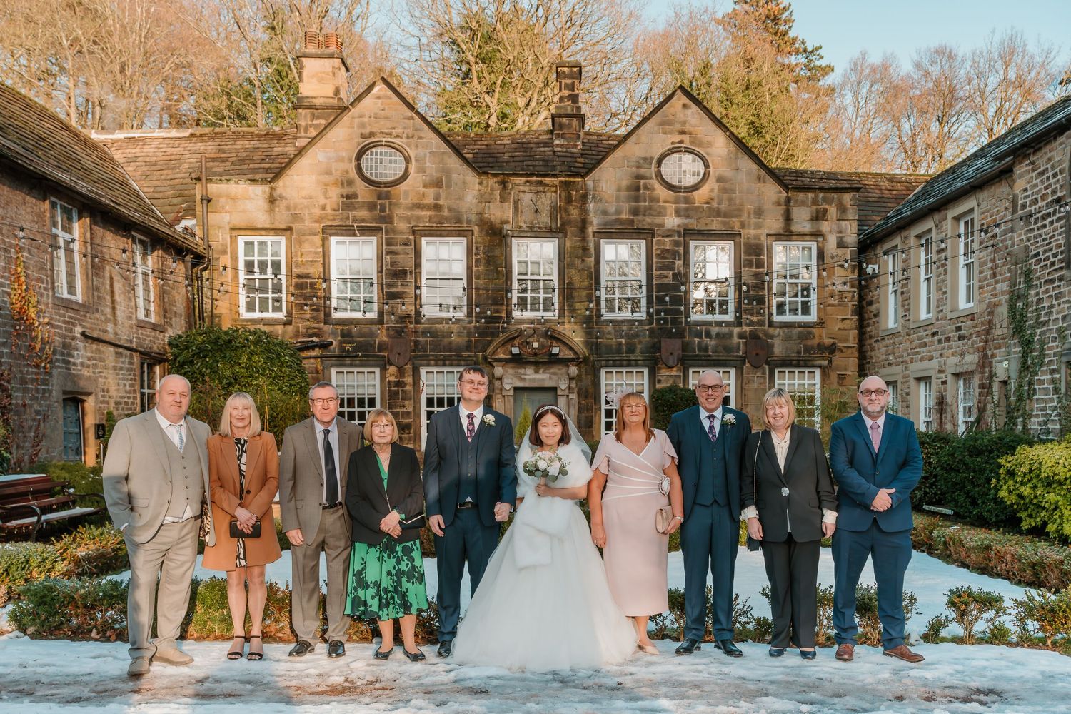 Large wedding party group photo outside rustic stone venue in snowy winter setting. Whitley Hall Wedding