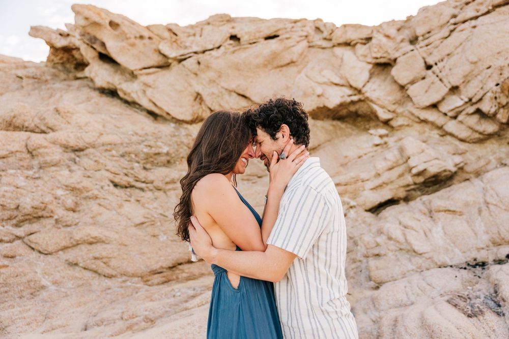 Romantic couple embracing and kissing near sandy rock formations in a desert landscape.