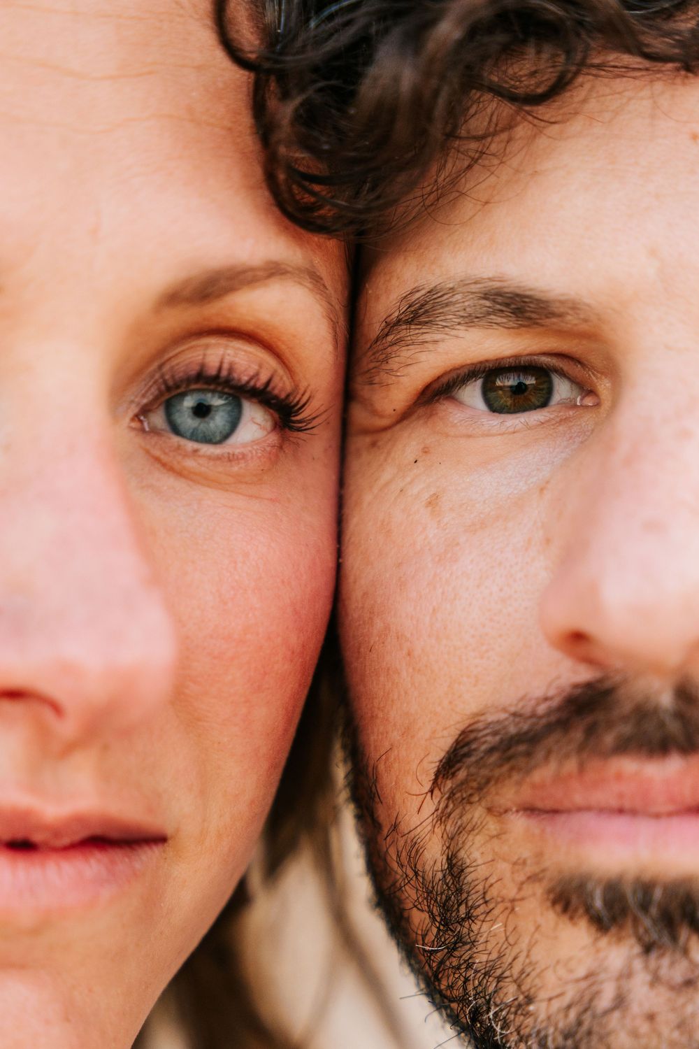 Close-up portrait of a man and woman with faces pressed together, showcasing blue and hazel eyes.