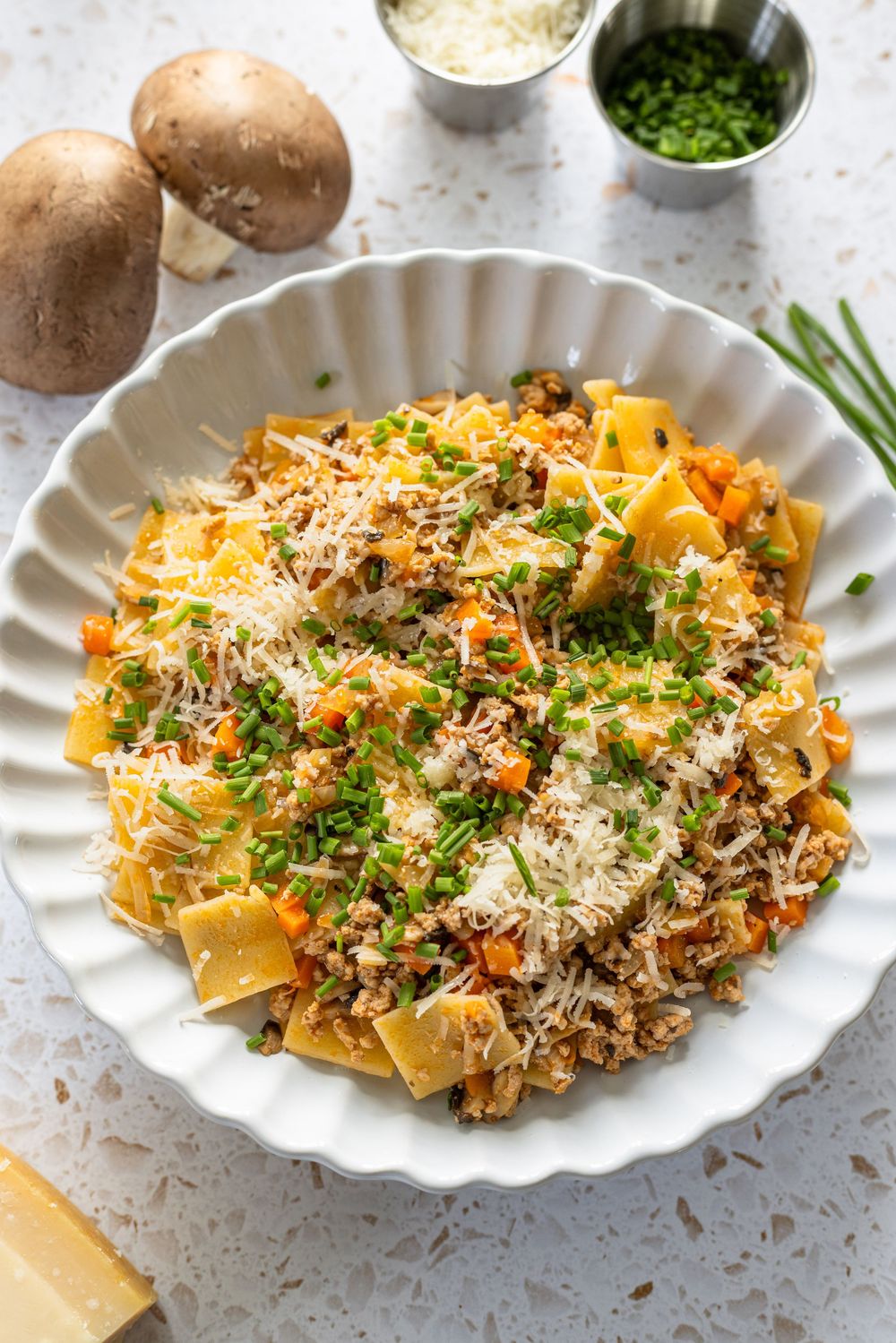 A bowl of pappardelle pasta with ground meat, carrots, mushrooms, topped with Parmesan and fresh chives.