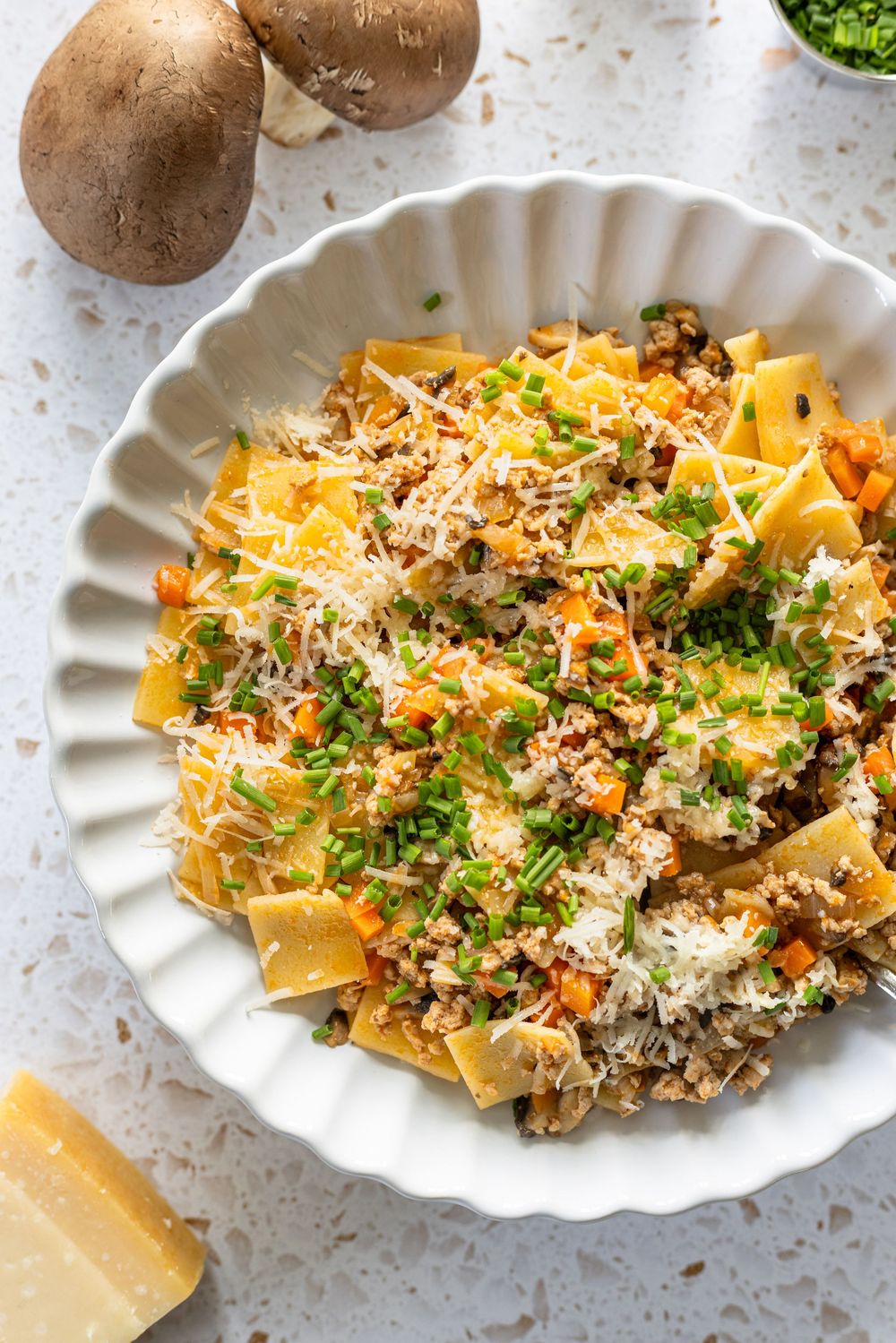A bowl of pappardelle pasta with mushroom bolognese, topped with grated Parmesan and fresh chives.
