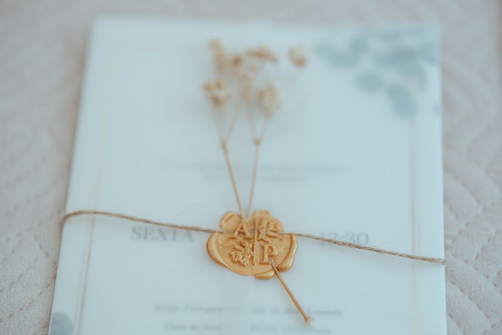 Elegant wedding invitation with gold wax seal and twine bow, adorned with dried flowers on white background.
