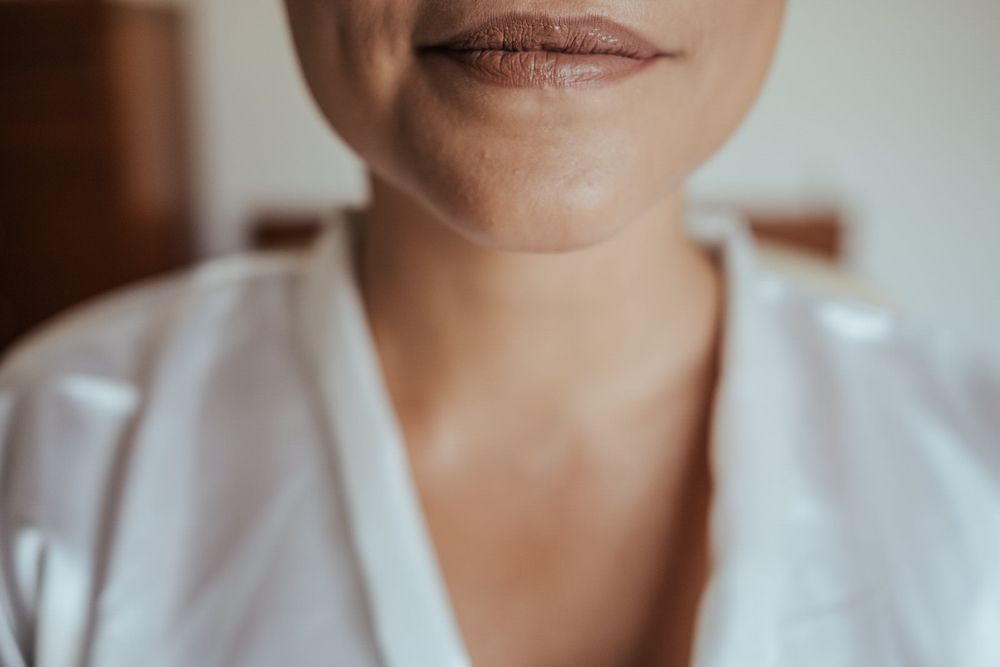 Close-up of a woman's lower face and neck, showcasing natural skin texture and subtle smile, wearing a white robe.