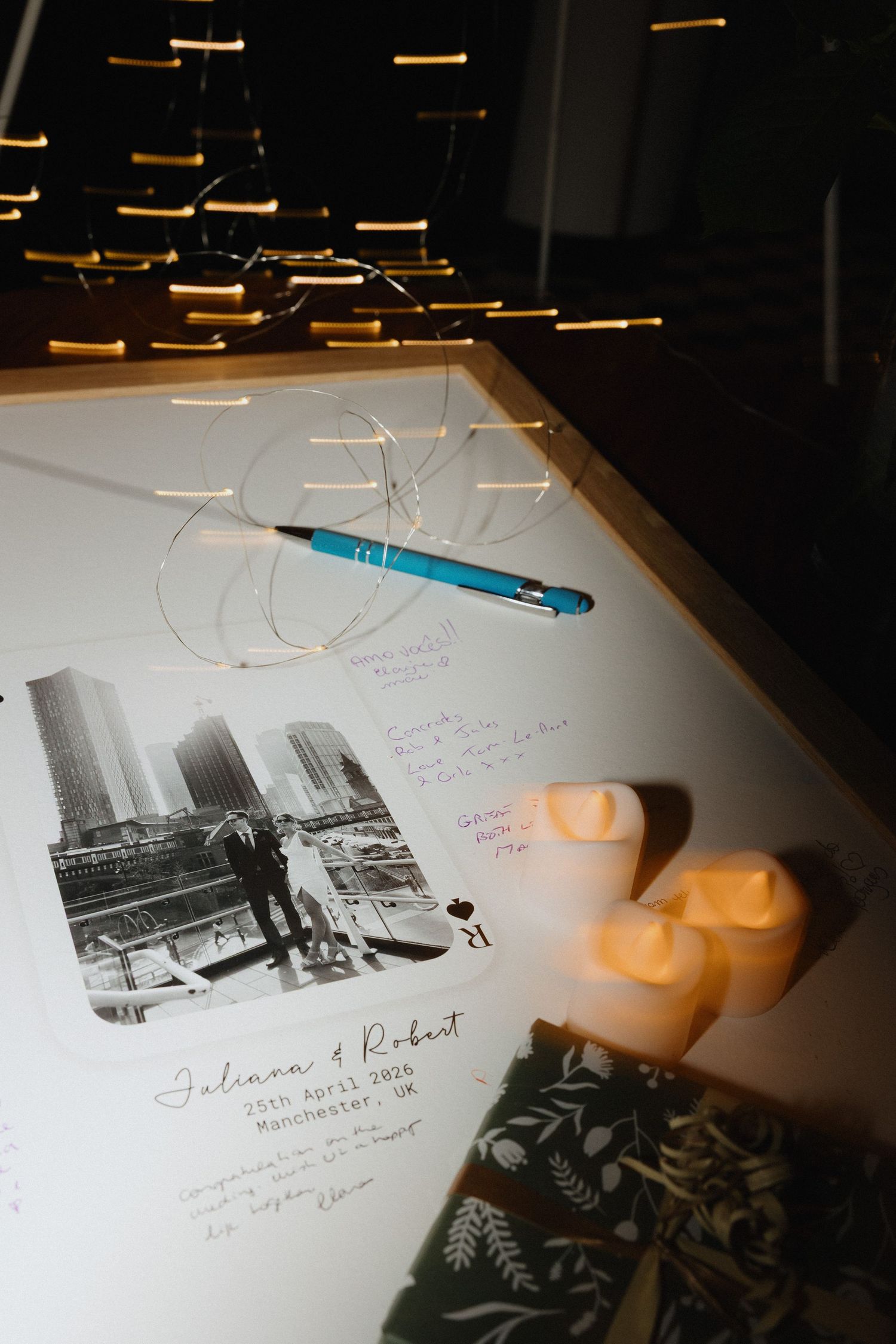 Wedding guest book with couple photo, candles, and blue pen on illuminated table at Johnson and Robert Manchester UK wedding.