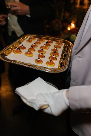 Gloved waiter serves elegant blini appetizers with caviar on gold tray at wedding reception.