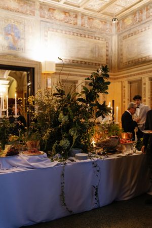 Elegant wedding reception buffet table with lush greenery arrangements in ornate frescoed venue.