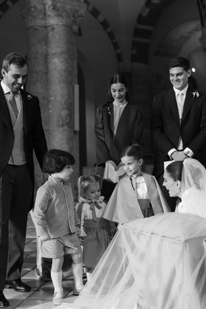 Black and white photo of bride greeting children in wedding party inside historic church.