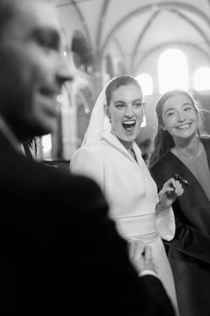 Black and white photo of joyful bride laughing with guest inside elegant arched church.