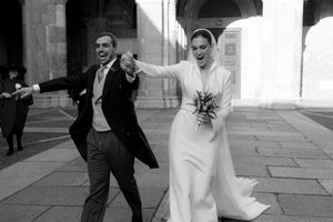 Black and white photo of a joyful bride and groom exiting a grand building, bride holding bouquet.