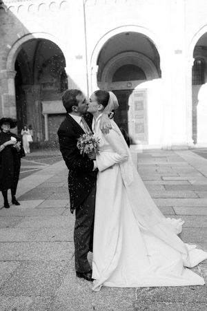 Black and white photo of a bride and groom sharing a kiss outside a historic building on their wedding day.