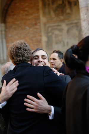 Smiling groom embracing wedding guest outside historic brick church during celebration.
