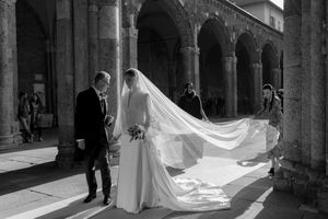 Black and white wedding photo of bride and groom walking under stone arches, veil flowing dramatically behind them.
