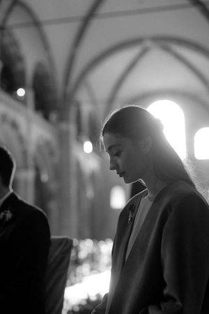 Black and white portrait of bride bowing head in prayer inside Gothic cathedral.