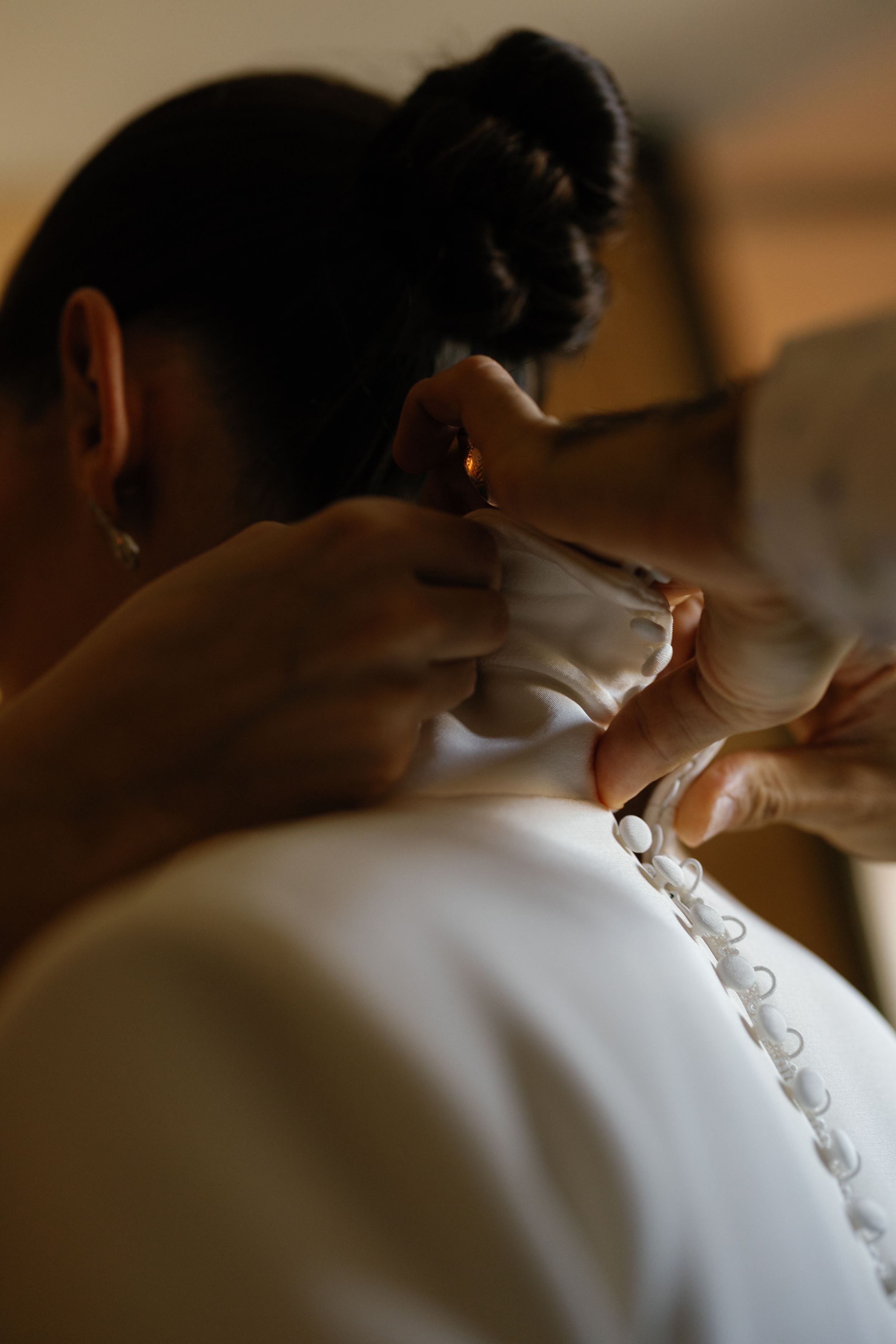 Close-up of hands fastening pearl buttons on back of elegant white wedding dress.