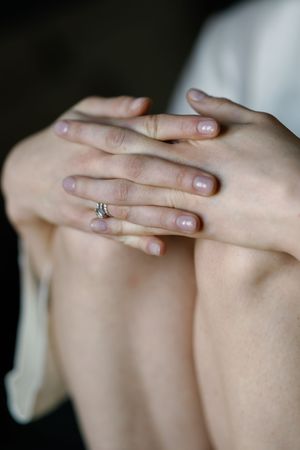 Close-up of a woman's hands resting on her knee, wearing a delicate diamond engagement ring.