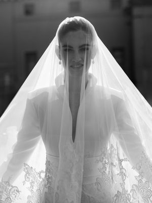 Black and white portrait of bride wearing long veil and white structured wedding dress outdoors.