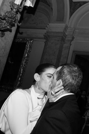 Black and white photo of a couple sharing a romantic kiss at an elegant wedding venue with ornate architecture.