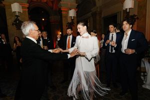Elegant wedding guests dancing at formal reception, woman in white fringe dress shaking hands with older gentleman.