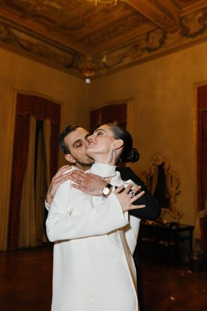 Couple shares romantic first dance embrace in ornate golden ballroom at wedding reception.