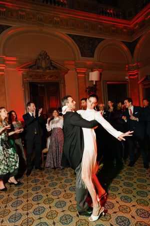 Couple performing dramatic tango dance in white fringe dress at elegant ballroom event with red ambient lighting.