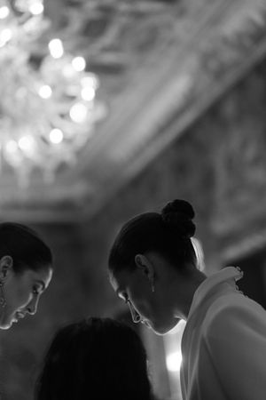 Black and white portrait of bride with updo hairstyle beneath ornate chandelier.