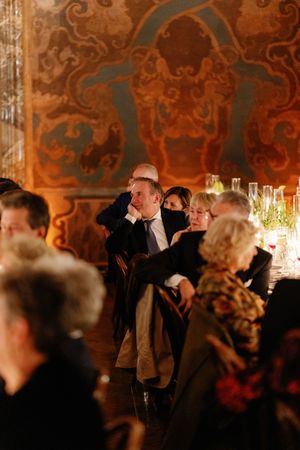 Wedding guest seated at reception dinner before ornate baroque painted wall mural.