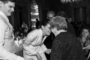 Black and white photo of bride leaning in to greet elderly guest at wedding reception.
