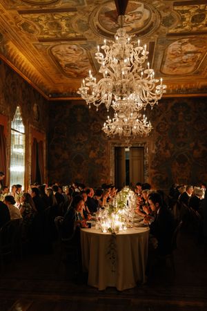 Elegant wedding reception in ornate room with frescoed ceiling, crystal chandeliers, and candlelit tables.