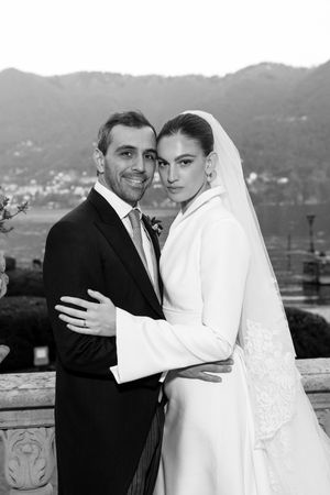 Black and white portrait of smiling bride and groom embracing with mountain lake backdrop.