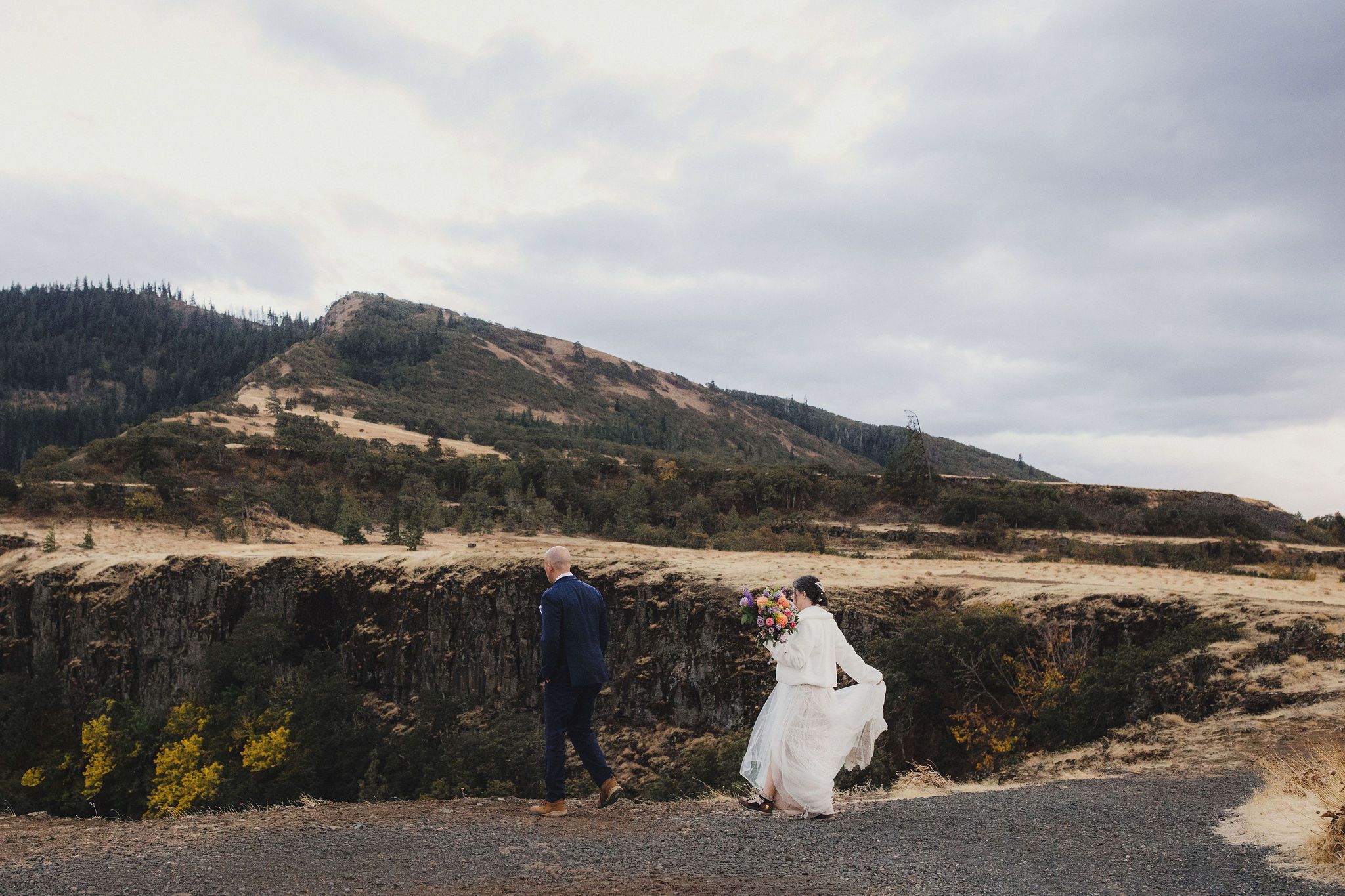 Bride and groom walking along rocky cliffside of Rowena Crest on a windy day.
