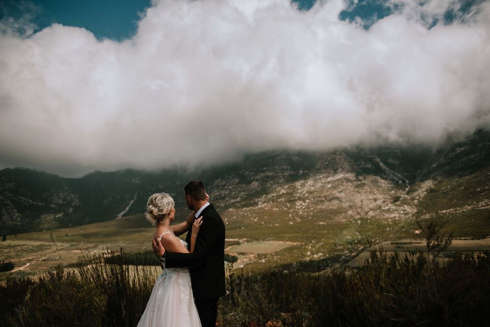 Newlyweds holding each other while looking out on the beautiful mountains and dramatic clouds at Imbeza Farm