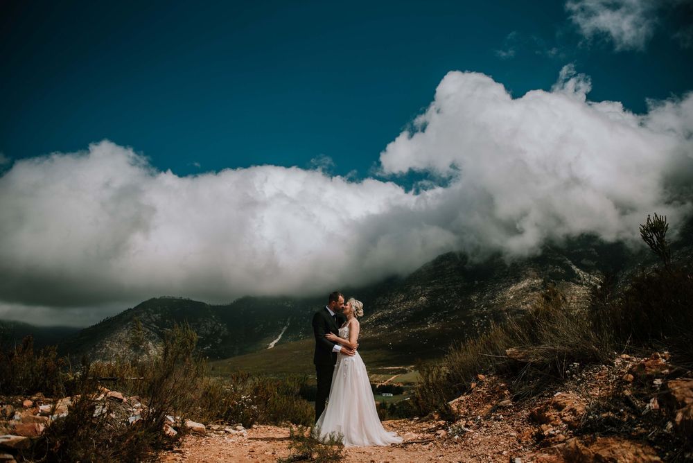 Romantic portrait of groom kissing his bride, with the mountains and dramatic clouds in the background.