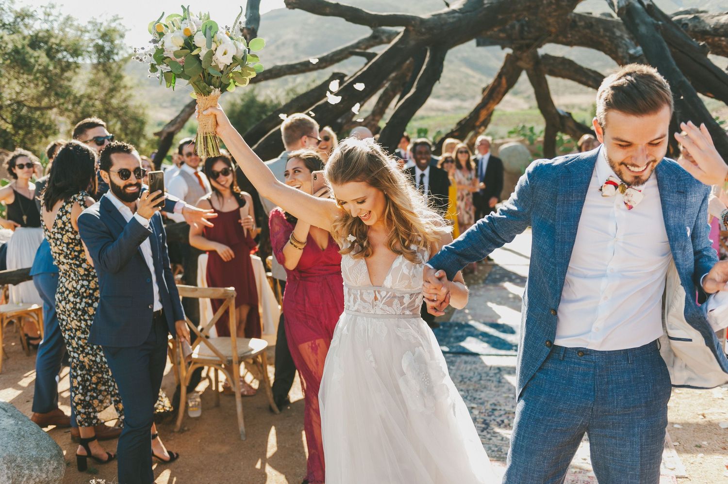 Joyful celebration with wedding guests dancing outdoors under rustic wooden beams during a garden reception.