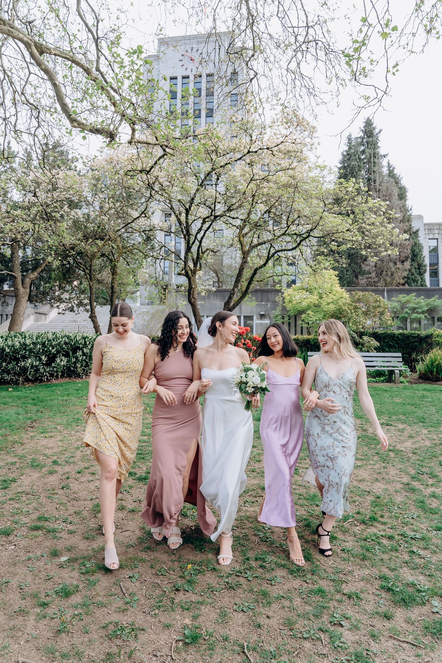 Wedding party walking together on grass wearing pastel and floral dresses in coordinated spring colors.