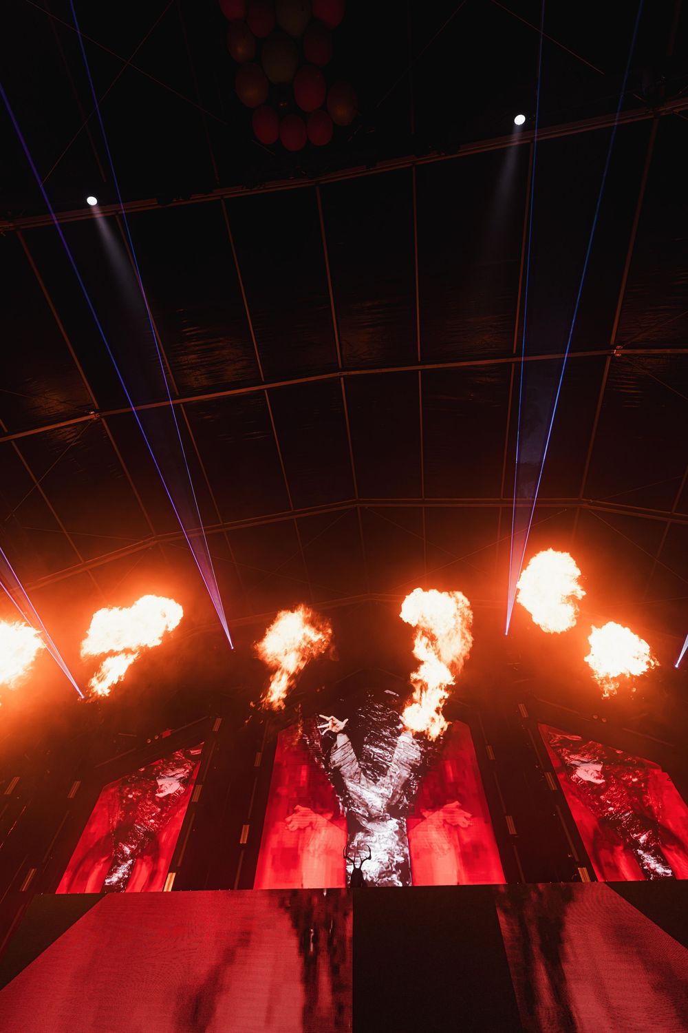 Fire bursts illuminate a dark stage with red lighting effects creating a dramatic performance atmosphere.