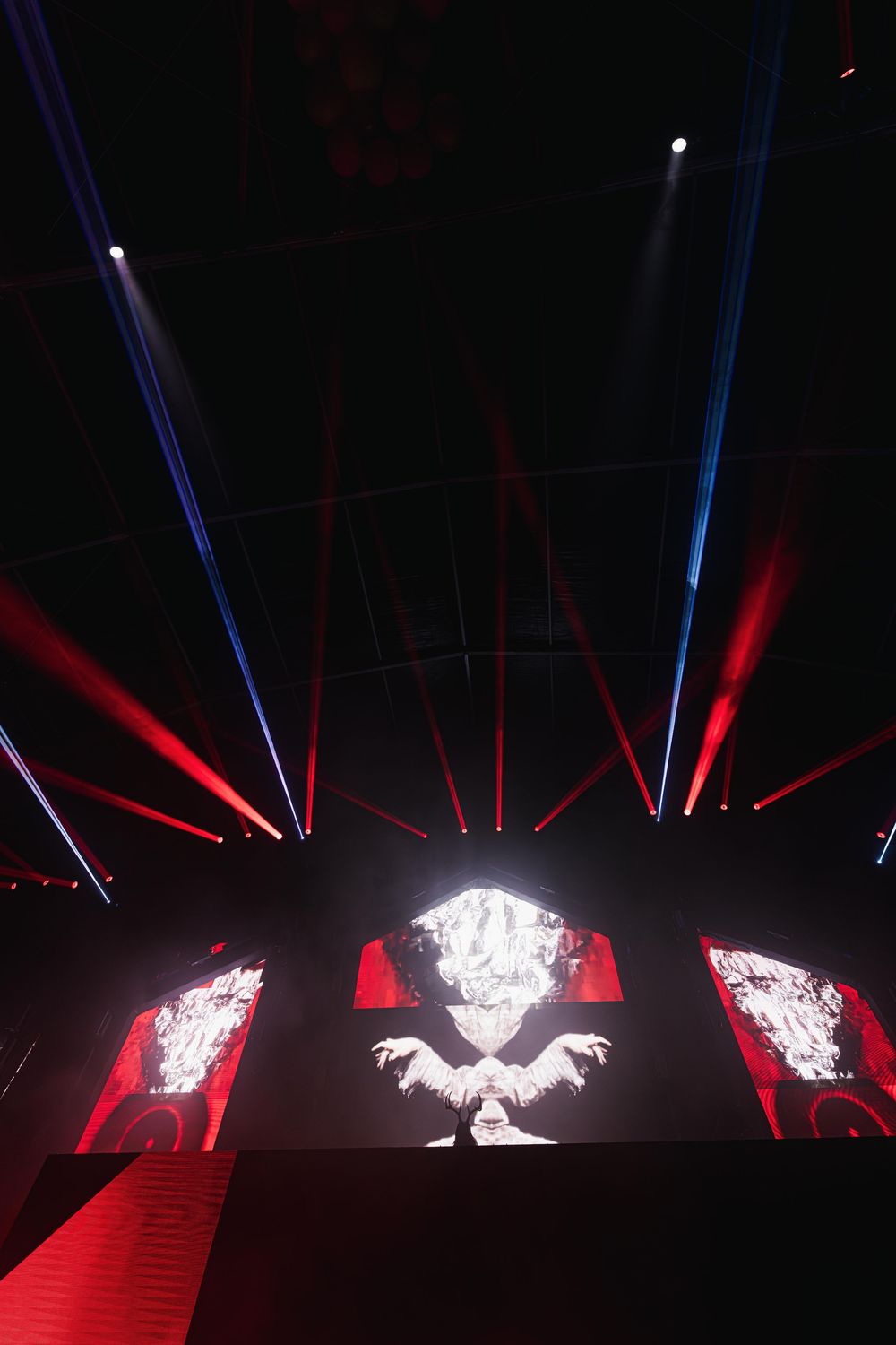 Dramatic stage performance with red and blue spotlights illuminating a dark arena with glowing white centerpiece display.