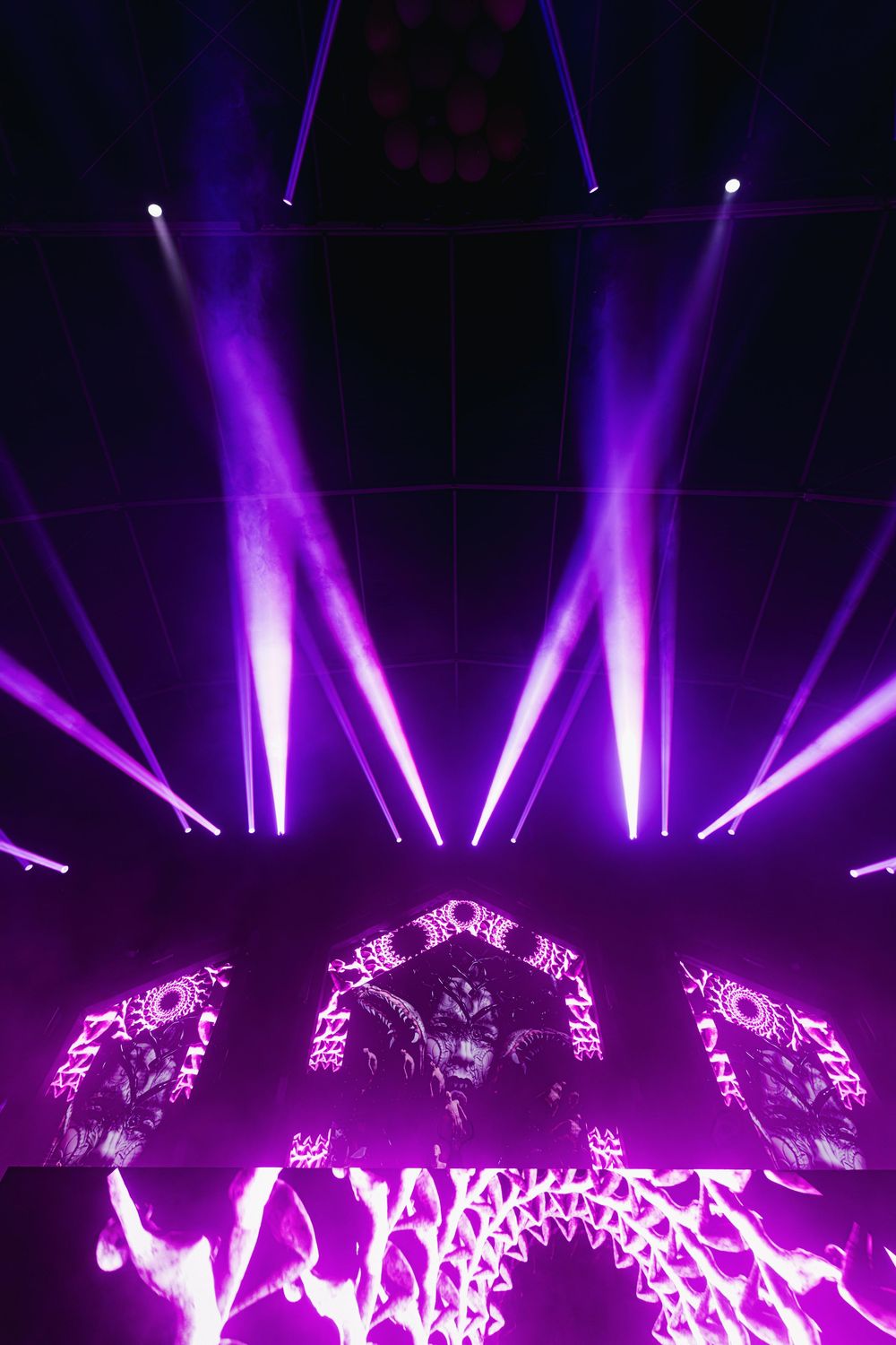 Purple stage lights create dramatic beams and patterns during a concert performance with dynamic lighting effects.