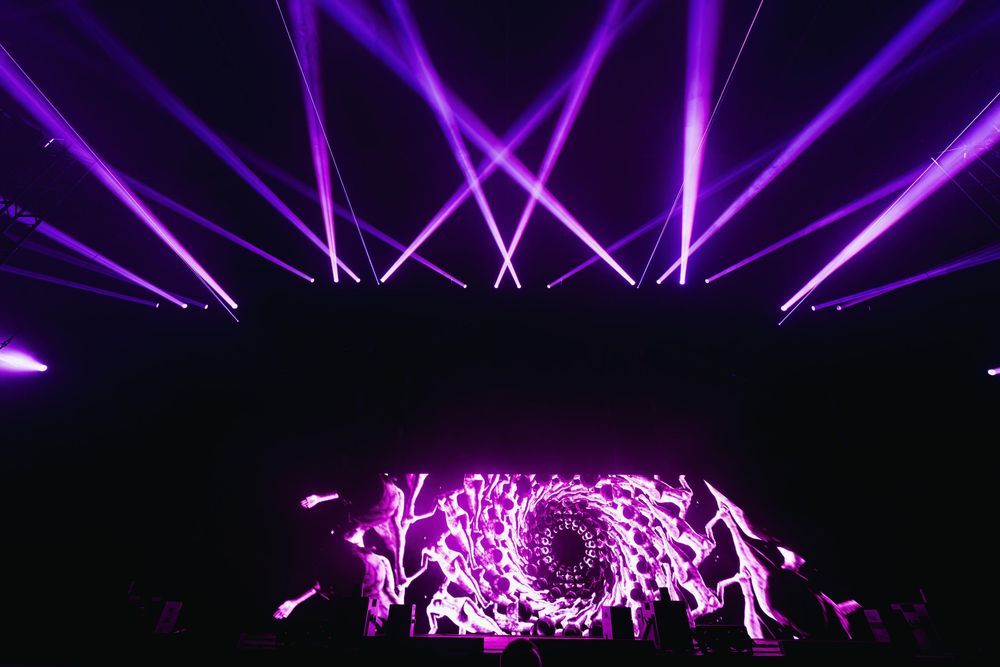 Vibrant purple laser beams illuminate a dark concert venue creating a dramatic lighting display during a performance.