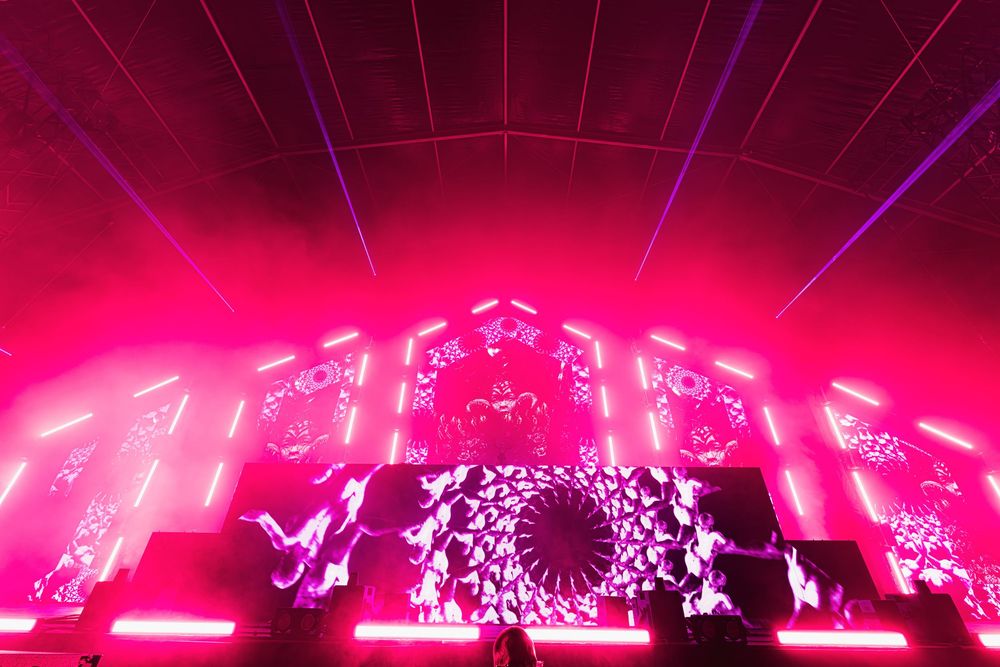 Concert stage illuminated with vibrant pink and purple lights creating a dynamic visual display during a live performance.