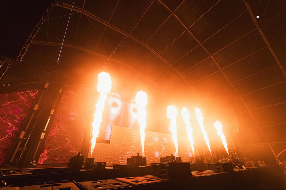 Pyrotechnic display illuminates dark concert stage with bright orange fireworks creating dramatic lighting effects.
