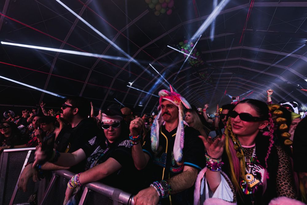 A crowded dance floor filled with people enjoying electronic music under colorful lights at a nightclub event.