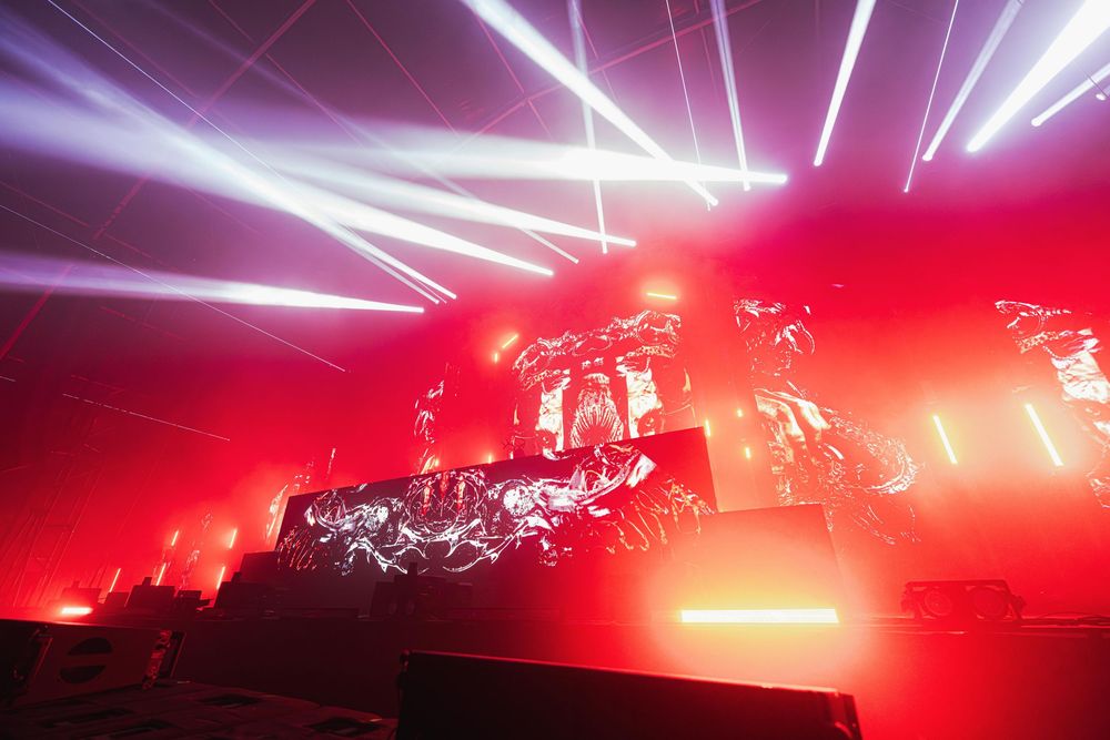 Concert stage illuminated with dramatic red and purple laser lights creating streaks across a dark atmosphere.