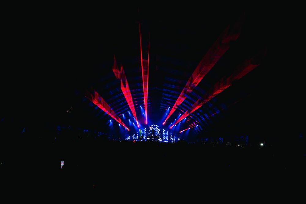 Colorful laser light show with red and blue beams illuminating a dark concert venue stage.