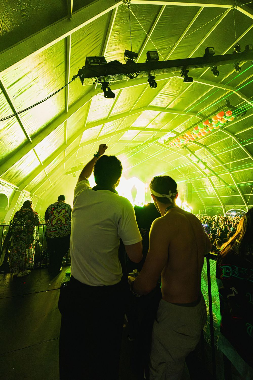 Silhouettes of people dancing in a tent illuminated with bright green lighting at a nighttime event.